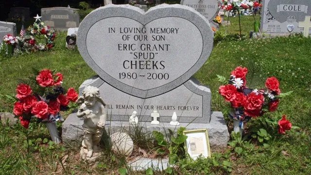 Eric Grant Cheeks' heart-shaped headstone in Silver Grove Cemetery, inscribed with 'In Loving Memory of Our Son Eric Grant "Spud" Cheeks, 1980–2000.' The grave is decorated with vibrant red and white flowers, small figurines, and a framed memorial tribute placed at the base.